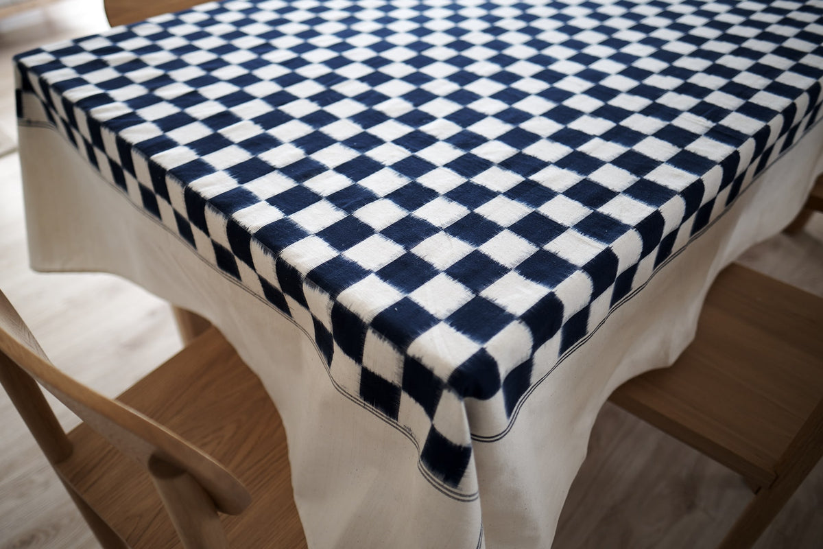 An Ikat Weave Tablecloth – Indigo Check by Stitchwallah on a wooden table.