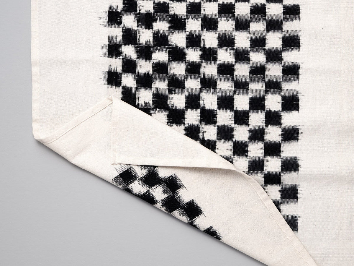 A Ikat Weave Tea-towel – Black Check towel by Stitchwallah on a white surface.