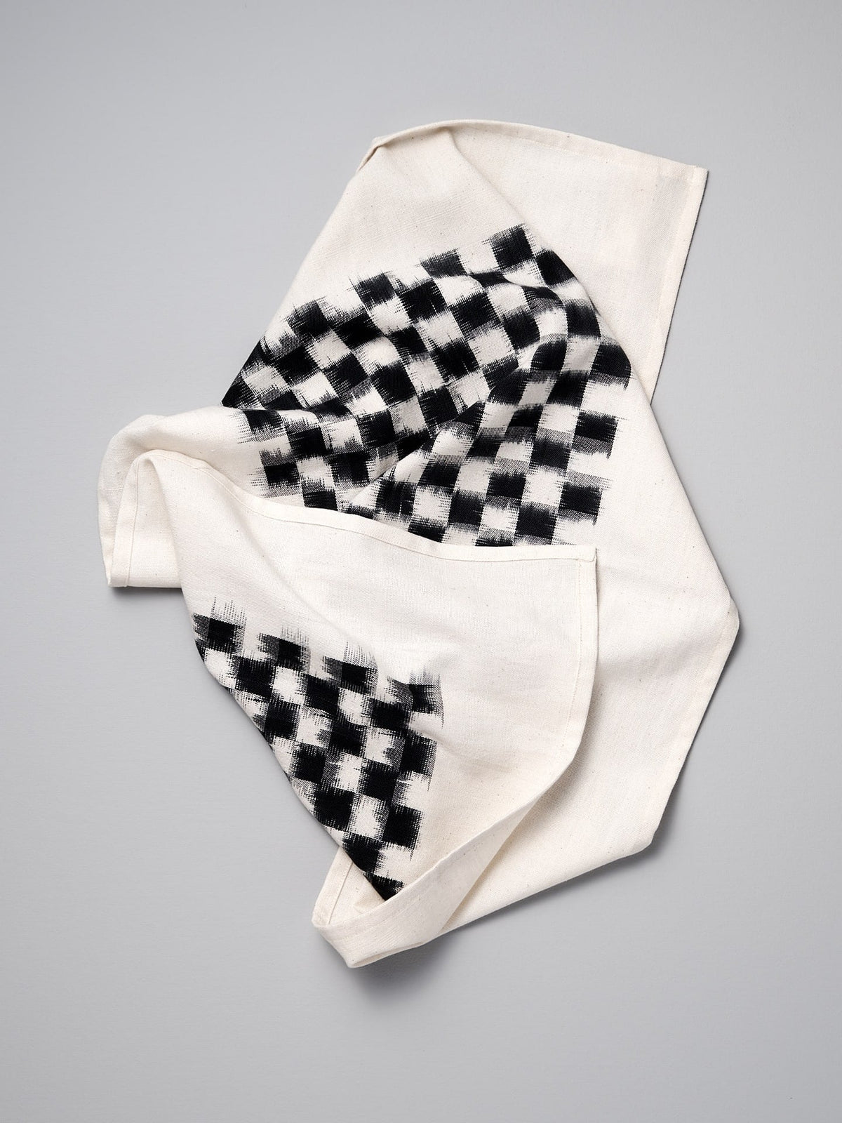 A Ikat Weave Tea-towel – Black Check handkerchief on a white surface from Stitchwallah.