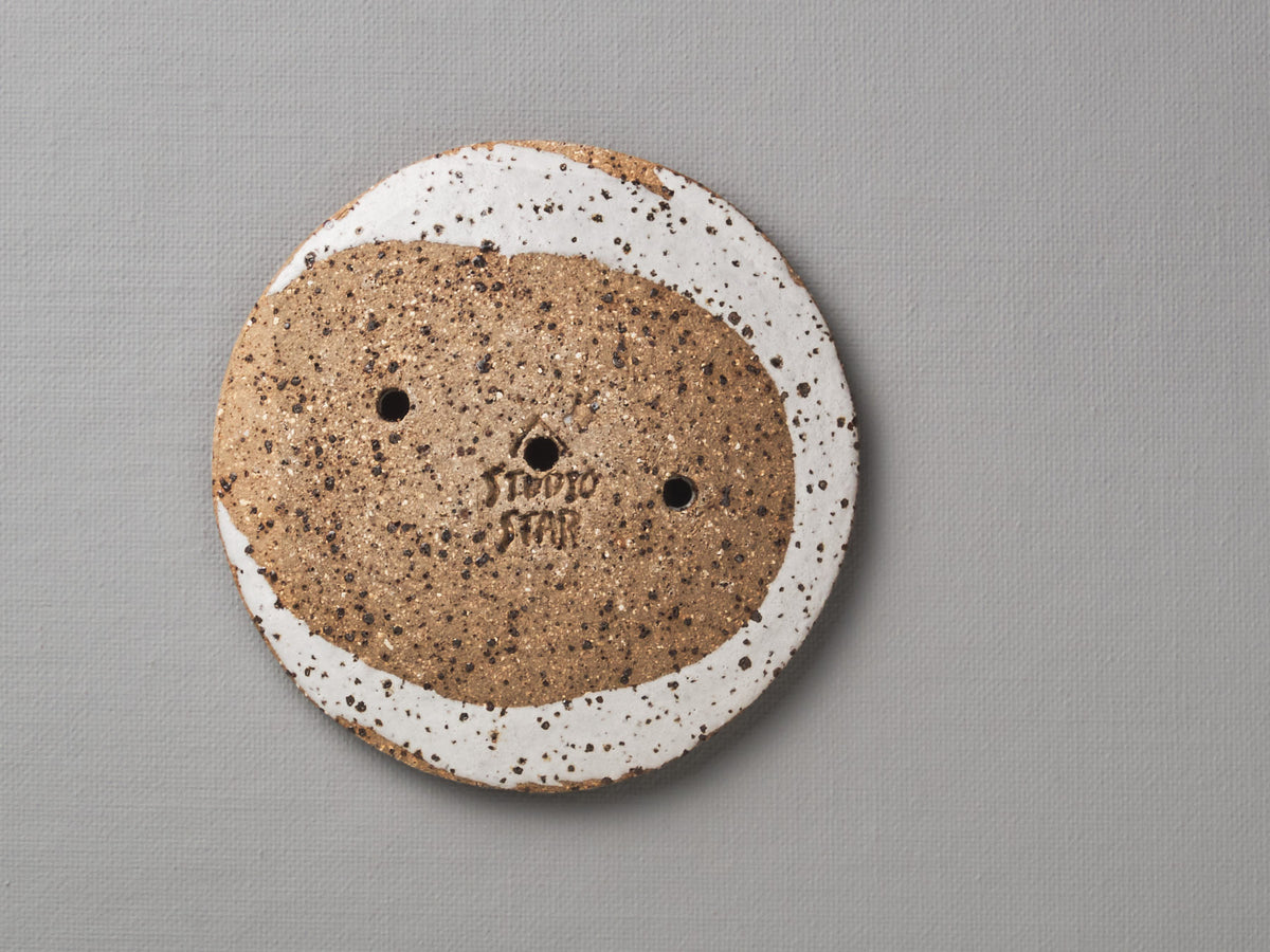 A Round Ceramic Soap Dish - White with Black Speckle by Studio Star with a brown and white circle on it.
