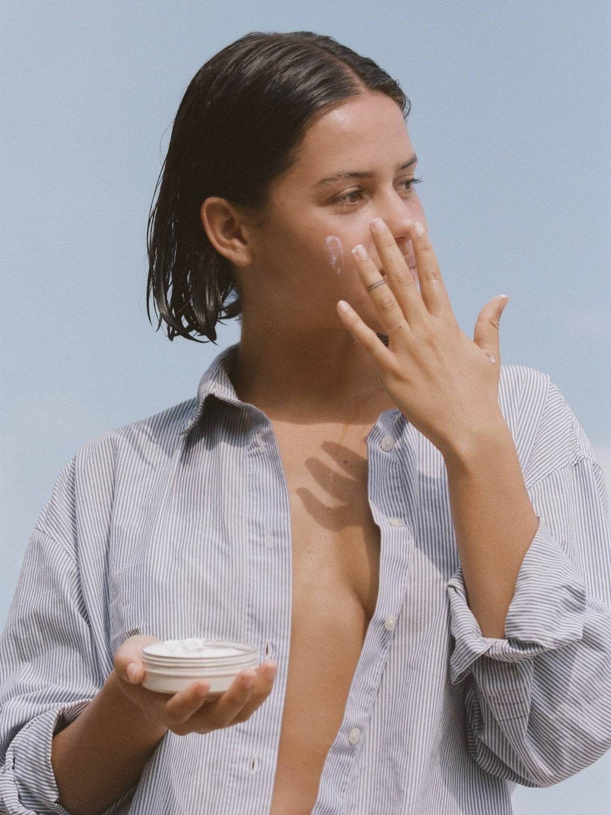 A woman in a blue shirt is holding a container of Sun Juju SPF50 Sunscreen for Face &amp; Body ⋅ Hydrating Reef Safe – 100𝚐.