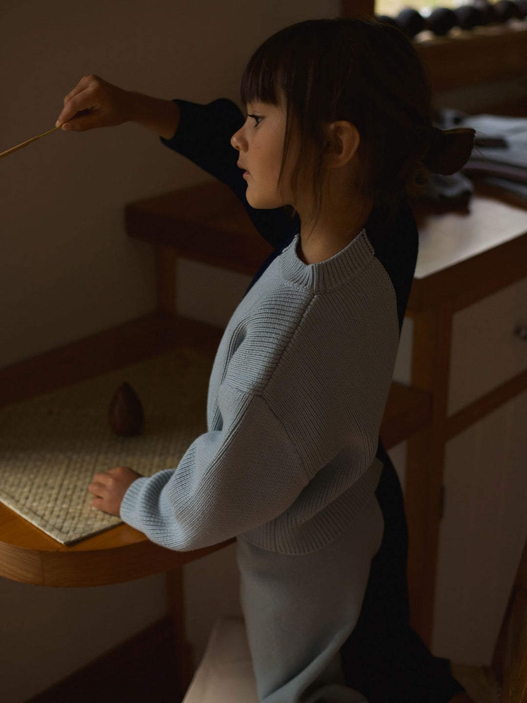 A little girl is sitting at a table with a Sol Sweater – Blue Multi by SUNNA STUDIOS in her hand.