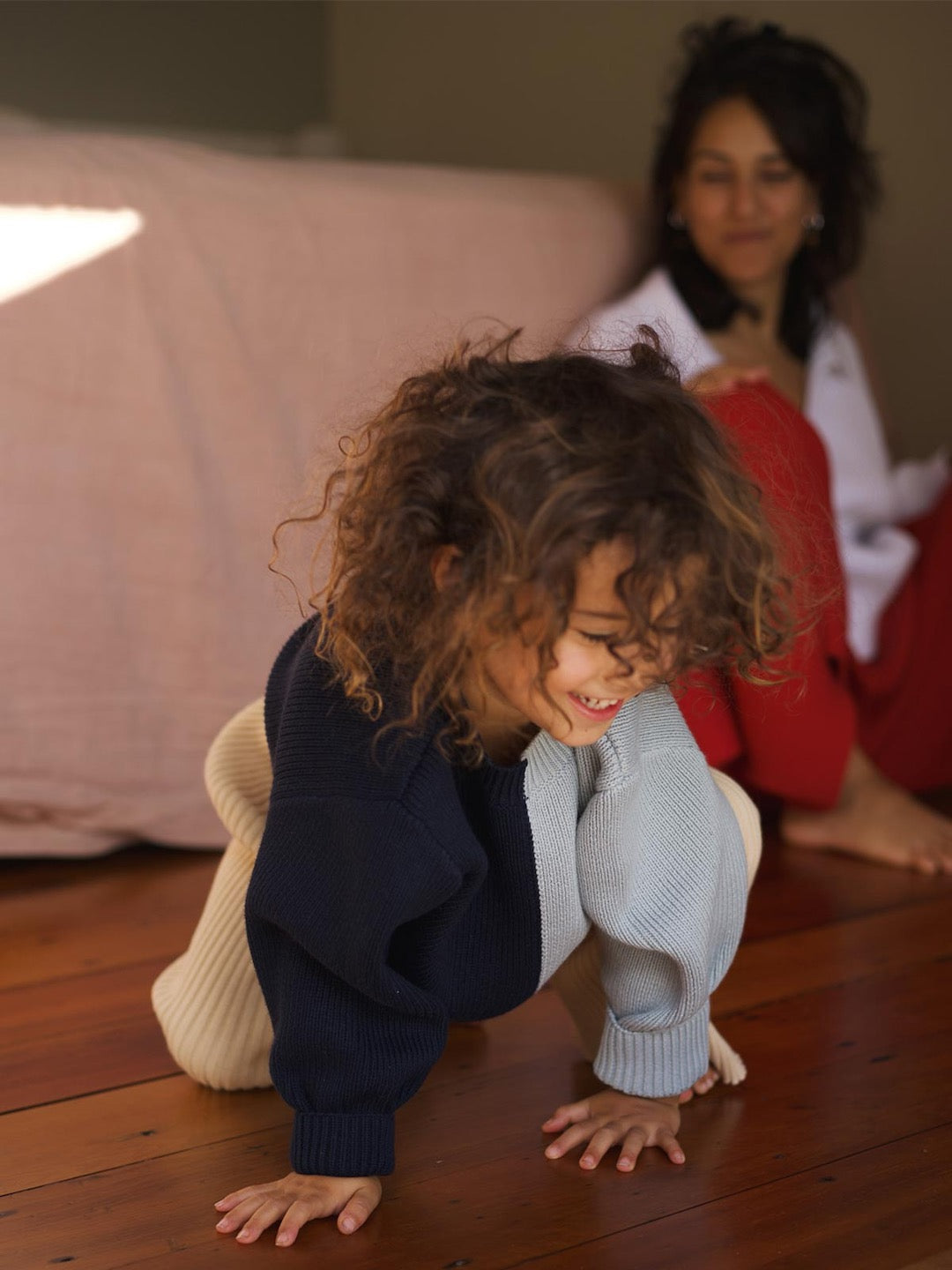 A little girl crawling on the floor wearing a Sol Sweater – Blue Multi from SUNNA STUDIOS.