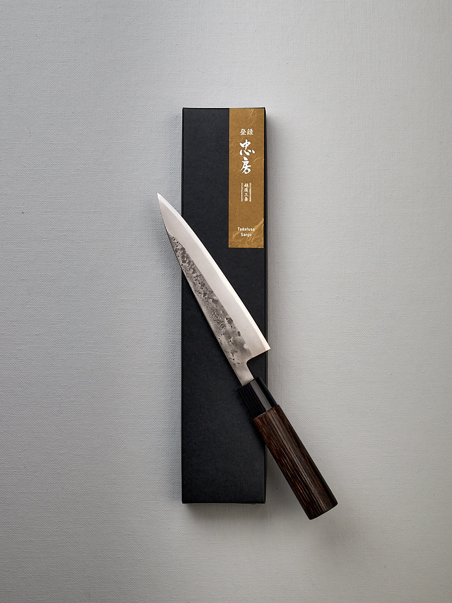 A Tadafusa Bocho Petty Knife in a box on a white surface.