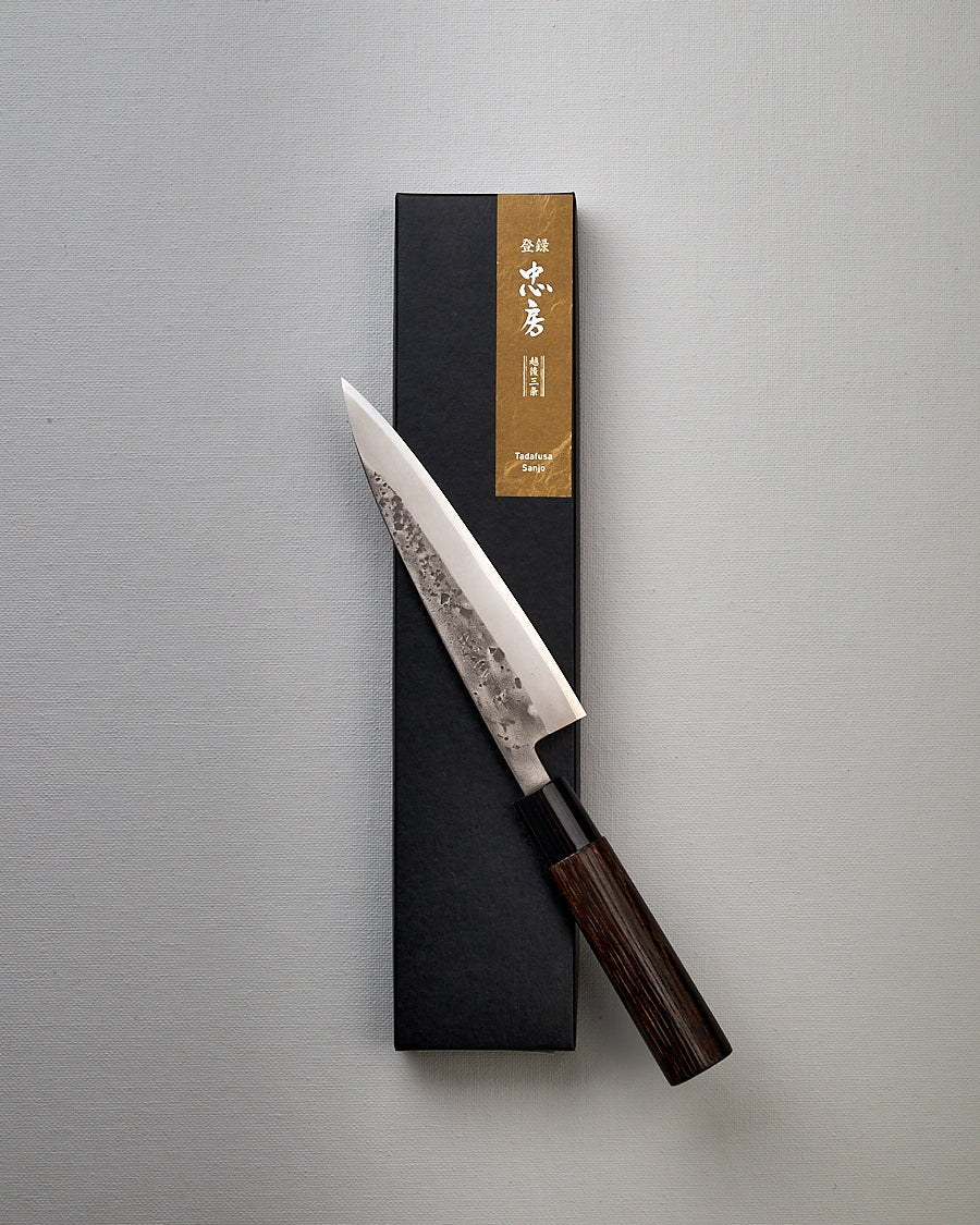 A Tadafusa Bocho Petty Knife in a box on a white surface.