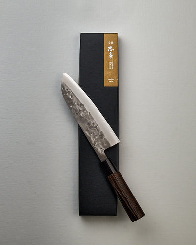 A Tadafusa Bocho Santoku Knife in a box on a white surface, suitable for all-purpose use with a focus on vegetables.