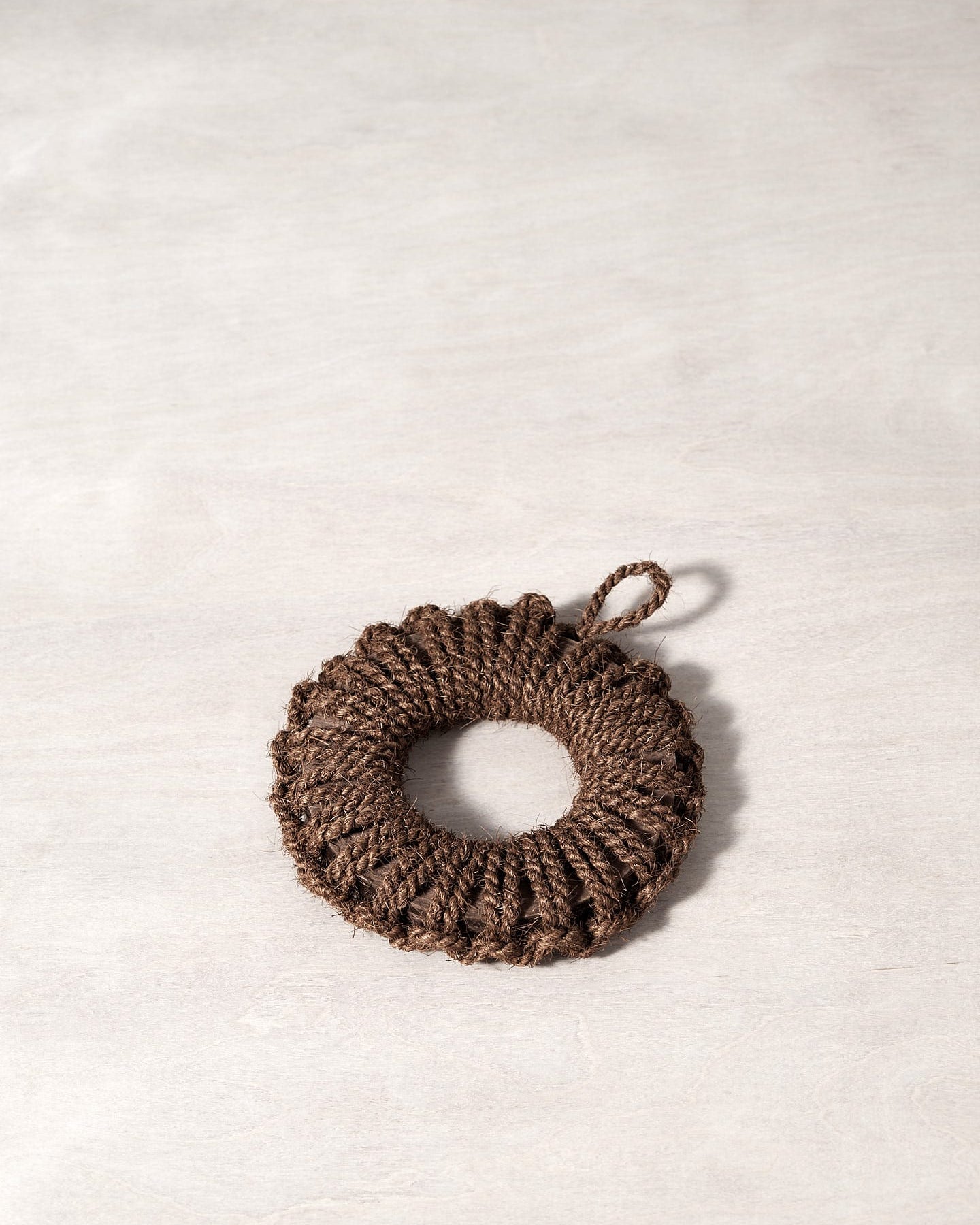 A Takada Hand-Knit Trivet – Small brown rope ornament on a white surface.