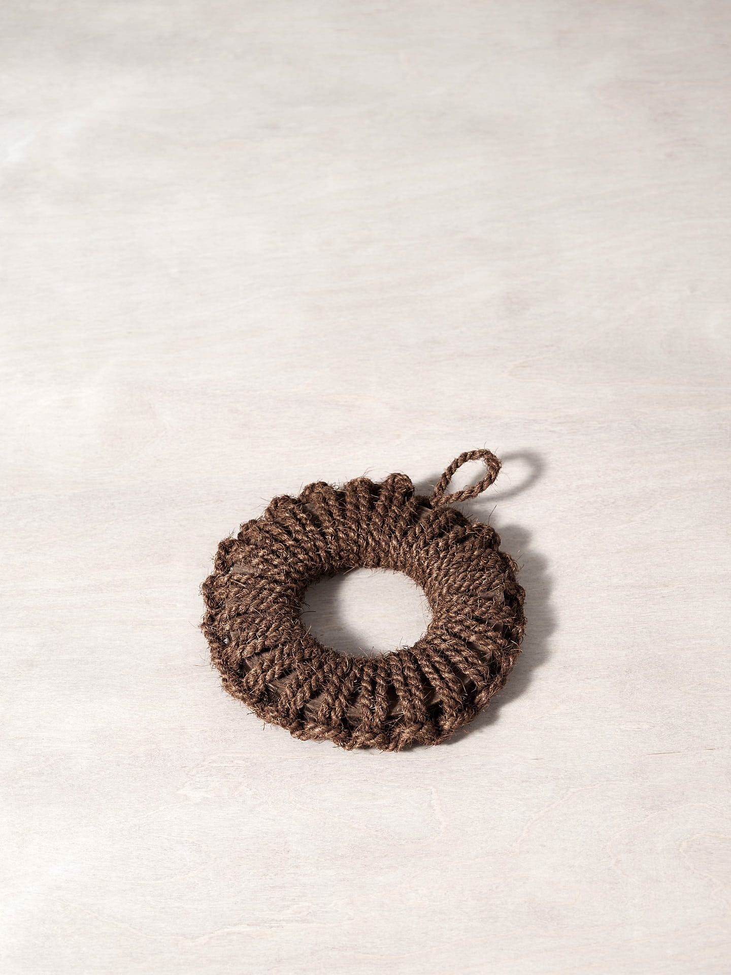 A Takada Hand-Knit Trivet – Small brown rope ornament on a white surface.