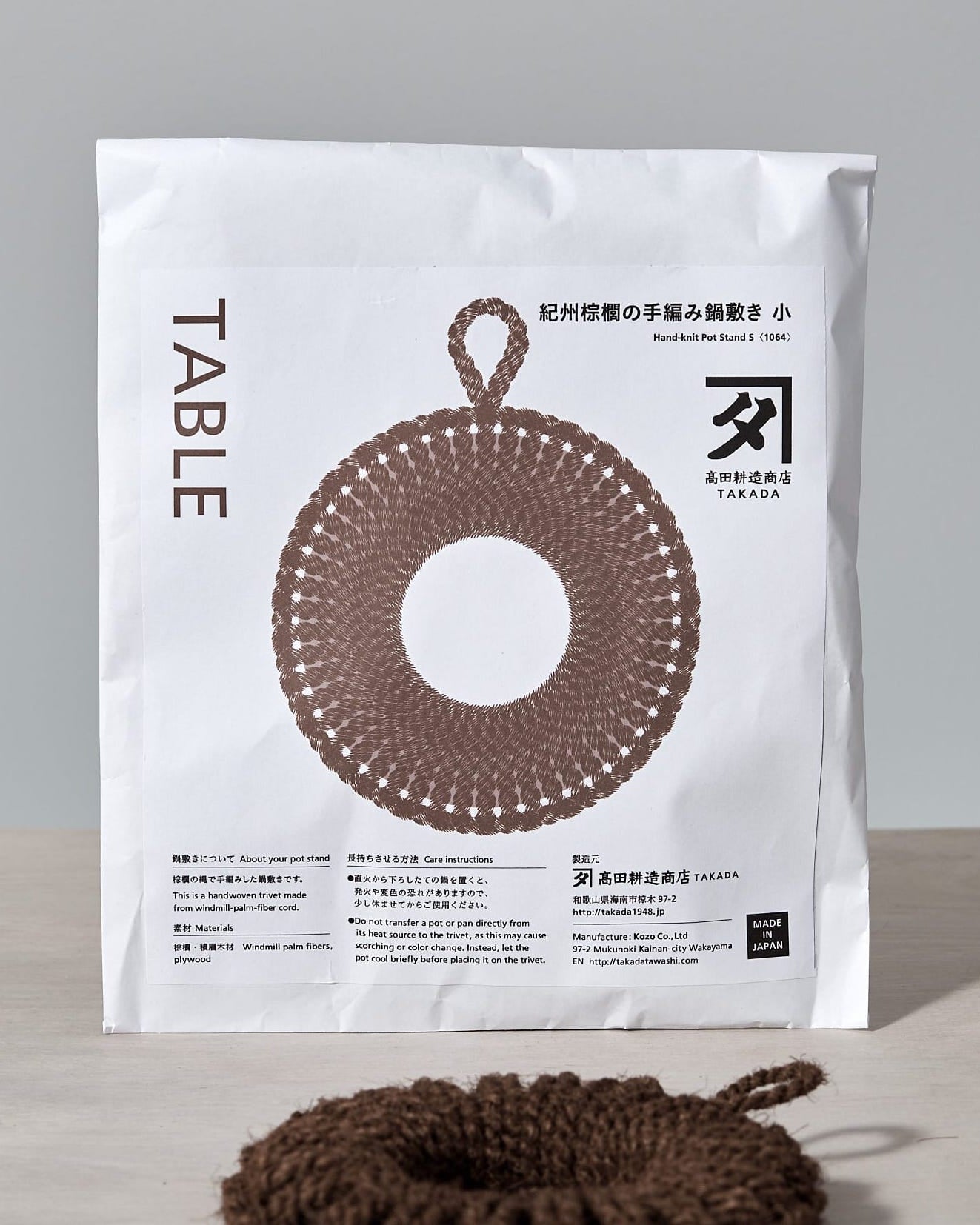 A Takada Hand-Knit Trivet – Small brown rope ornament on a white surface.