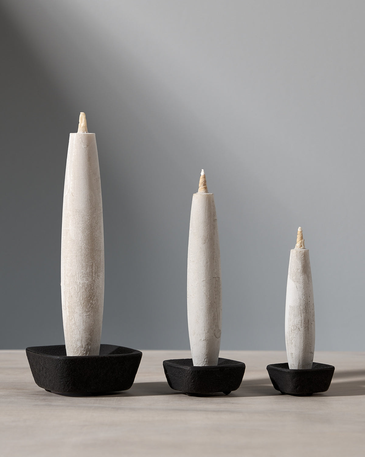 An elegant gift set featuring three Takazawa Tohaku – Small (8 piece box set) candles displayed on a table, enhanced by the unique Koma cast iron candle holder.