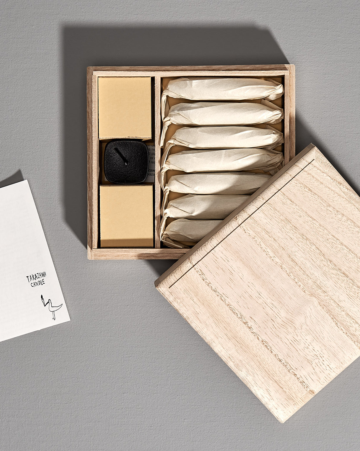 A box with an elegant gift set consisting of a Koma cast iron candle holder and Takazawa TOHAKU – Small (8 piece box set) candles sitting on top of it.