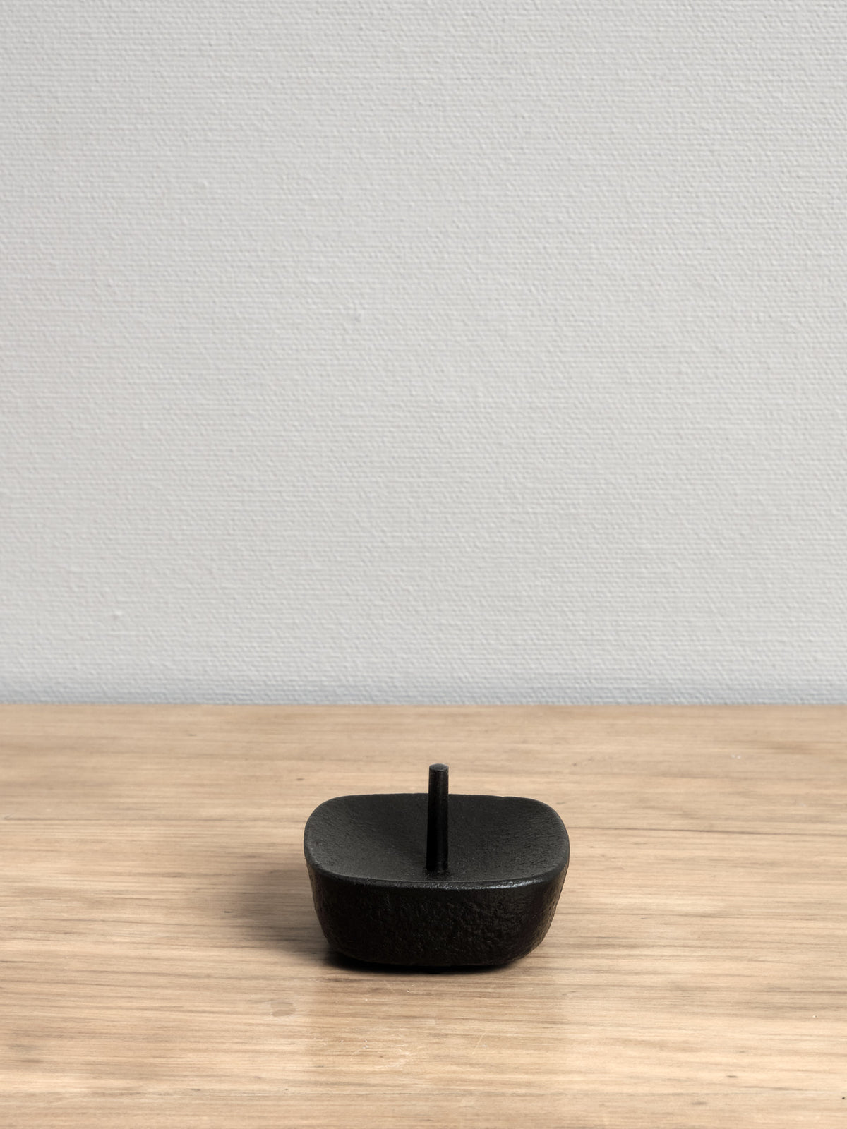 A Takazawa medium Koma Iron Candle Stand sitting on top of a wooden table.