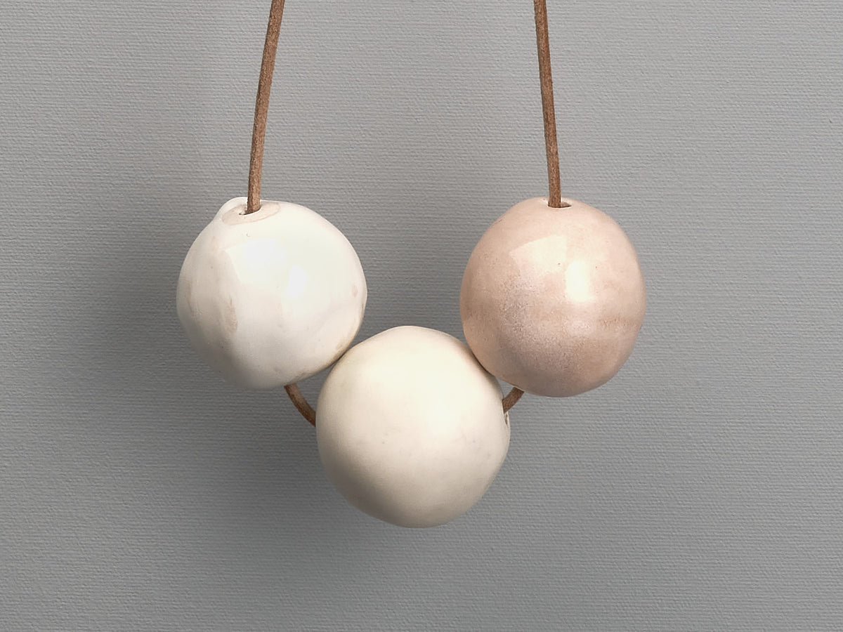 Three Tamara Rookes Ceramic Beads – Ø 50𝗆𝗆 hanging from a string on a gray background.