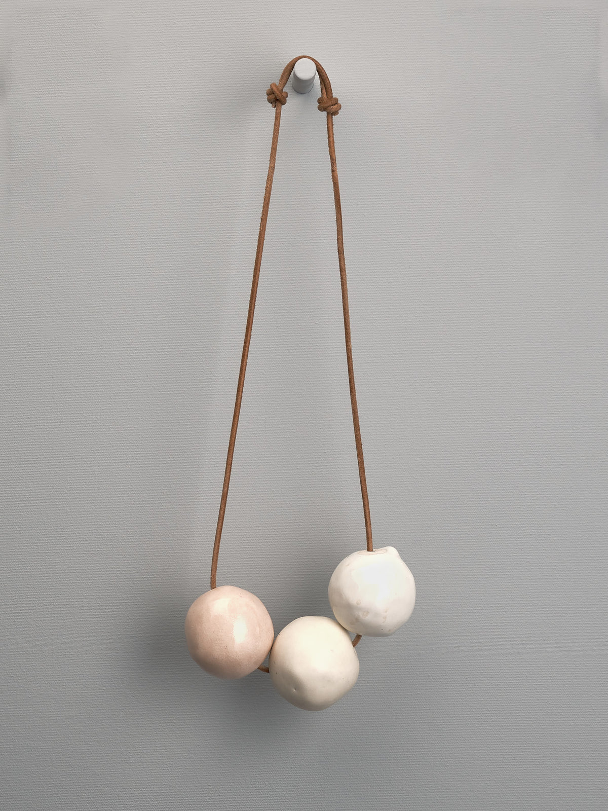 A Tamara Rookes necklace with three Ceramic Beads – Ø 50𝗆𝗆 hanging from a leather cord.