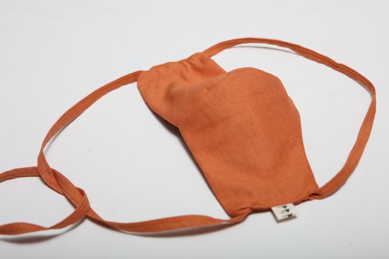 A small Linen Face Mask - Terracotta pouch on a white surface by Peppin.