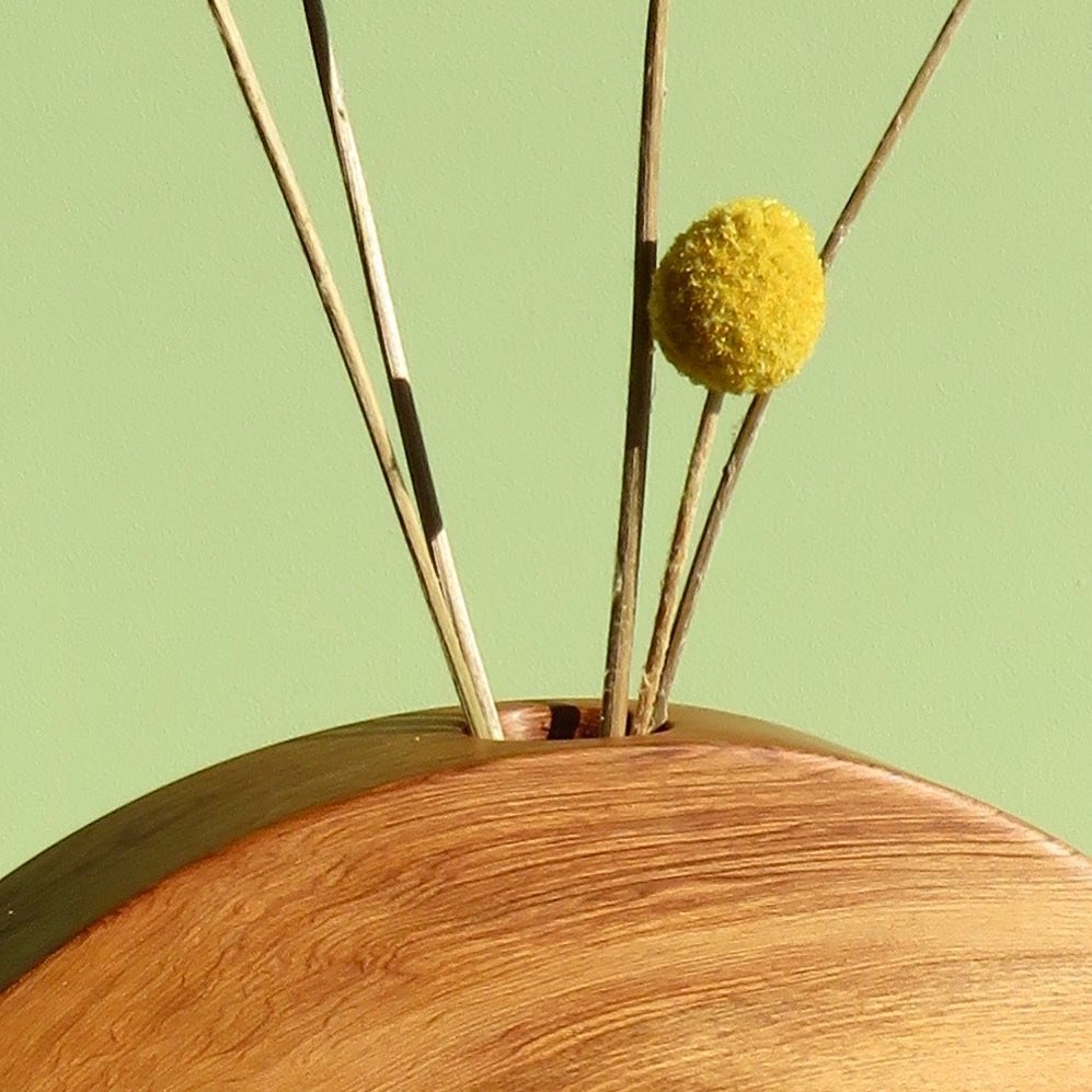 A The River Orb Candle Holder with two sticks and a yellow flower.