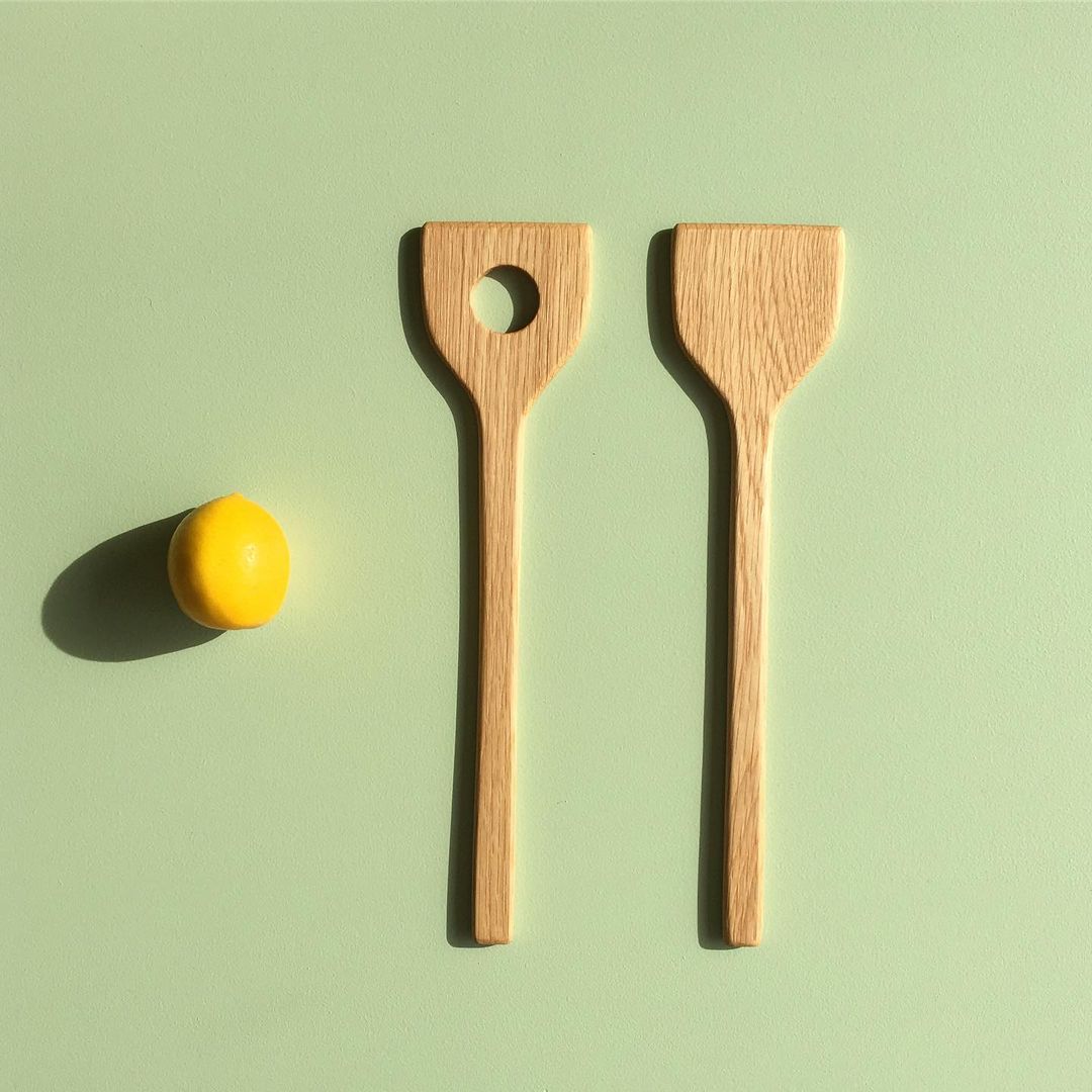 Two River wooden spoons next to a lemon on a green surface.