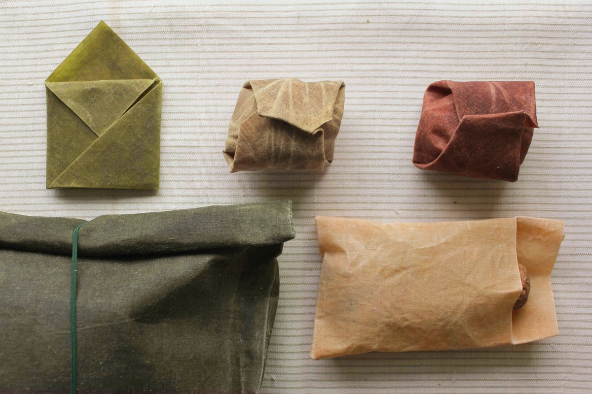 Assorted origami paper figures displayed on a textured surface, resembling Wax Atelier&#39;s Waxed Linen Food Wraps (Set of 3) in Ivy, Madder, and Indigo, sustainable alternative designs to plastic clingfilm.
