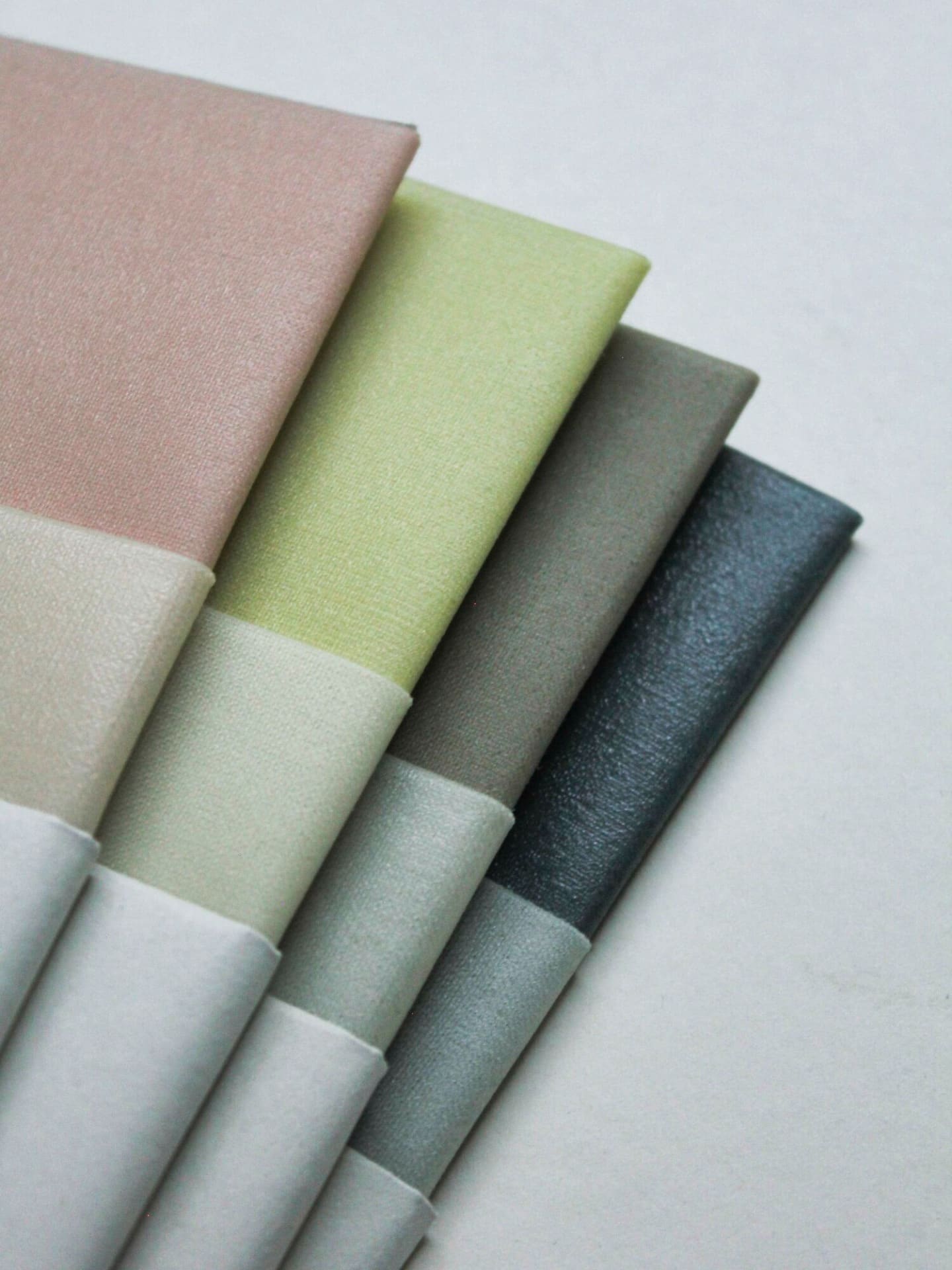 A selection of Ivy ⋄ Madder ⋄ Indigo Waxed Linen Food Wraps (Set of 3) in a gradient of colors from pink to dark gray, displayed in a fan arrangement by Wax Atelier.