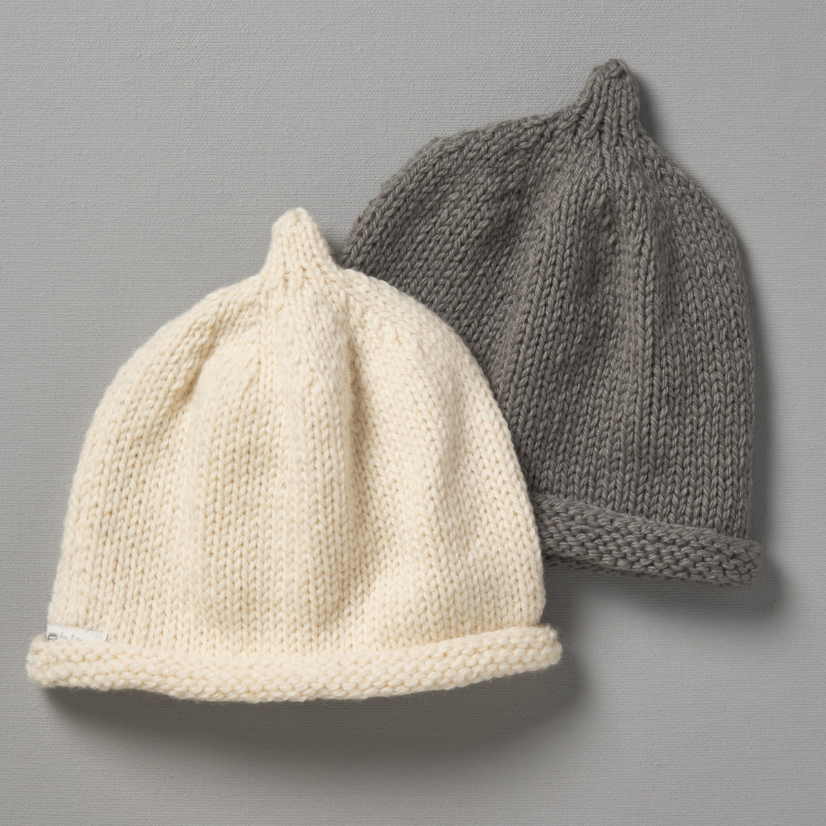 Two Hand Knitted Baby Beanies - Mushroom by Weebits on a grey surface.