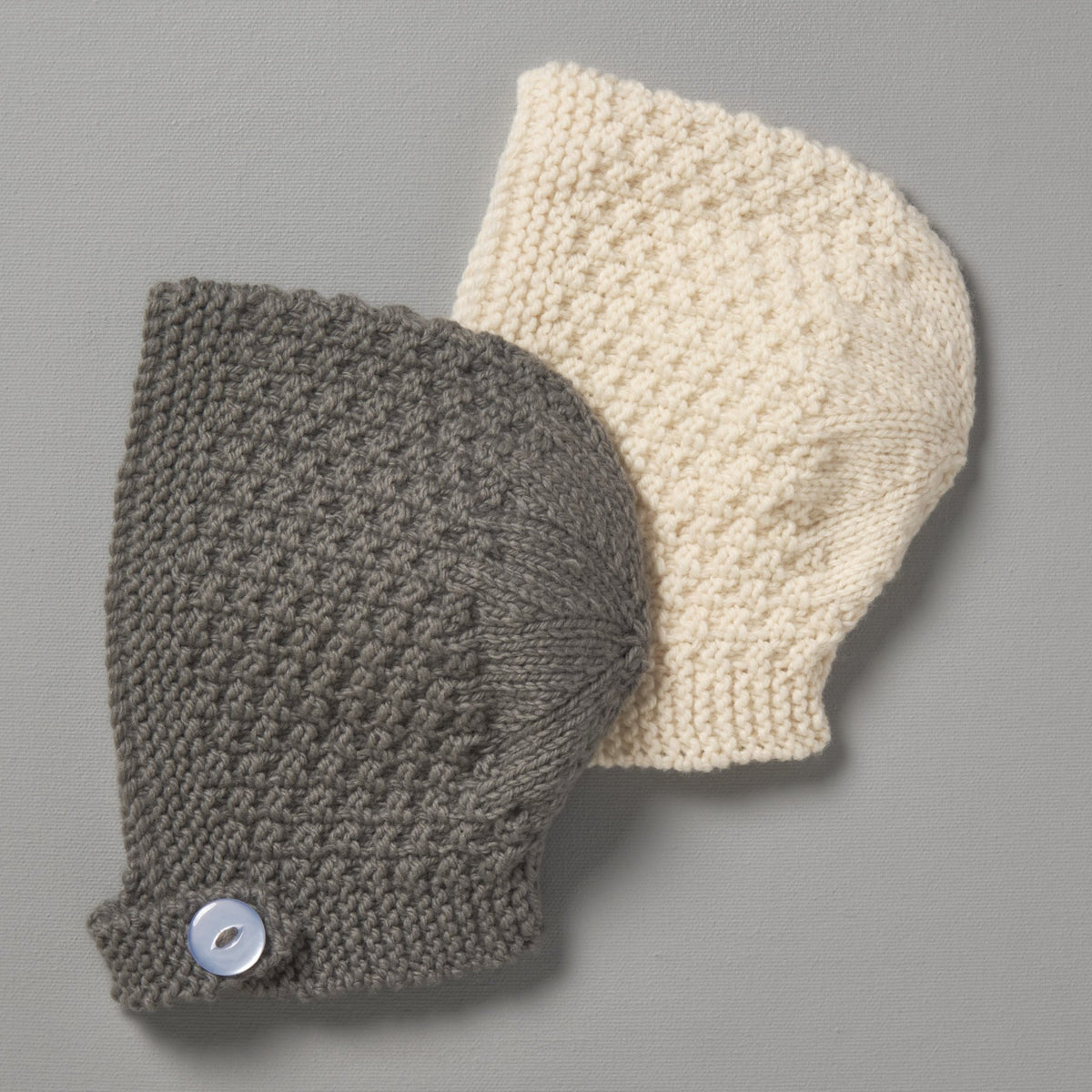 Two Weebits Hand Knitted Baby Bonnets on a gray surface.