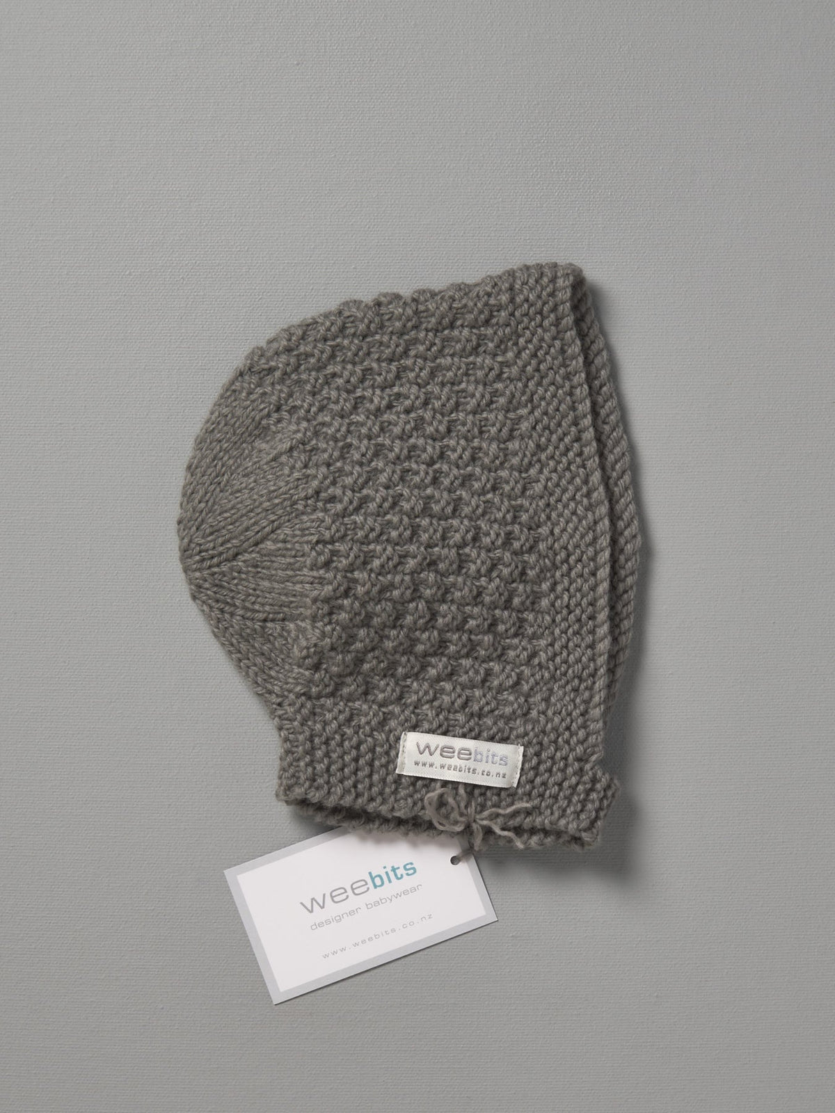 A grey Hand Knitted Baby Bonnet - Mushroom with a tag on it. (Brand: Weebits)