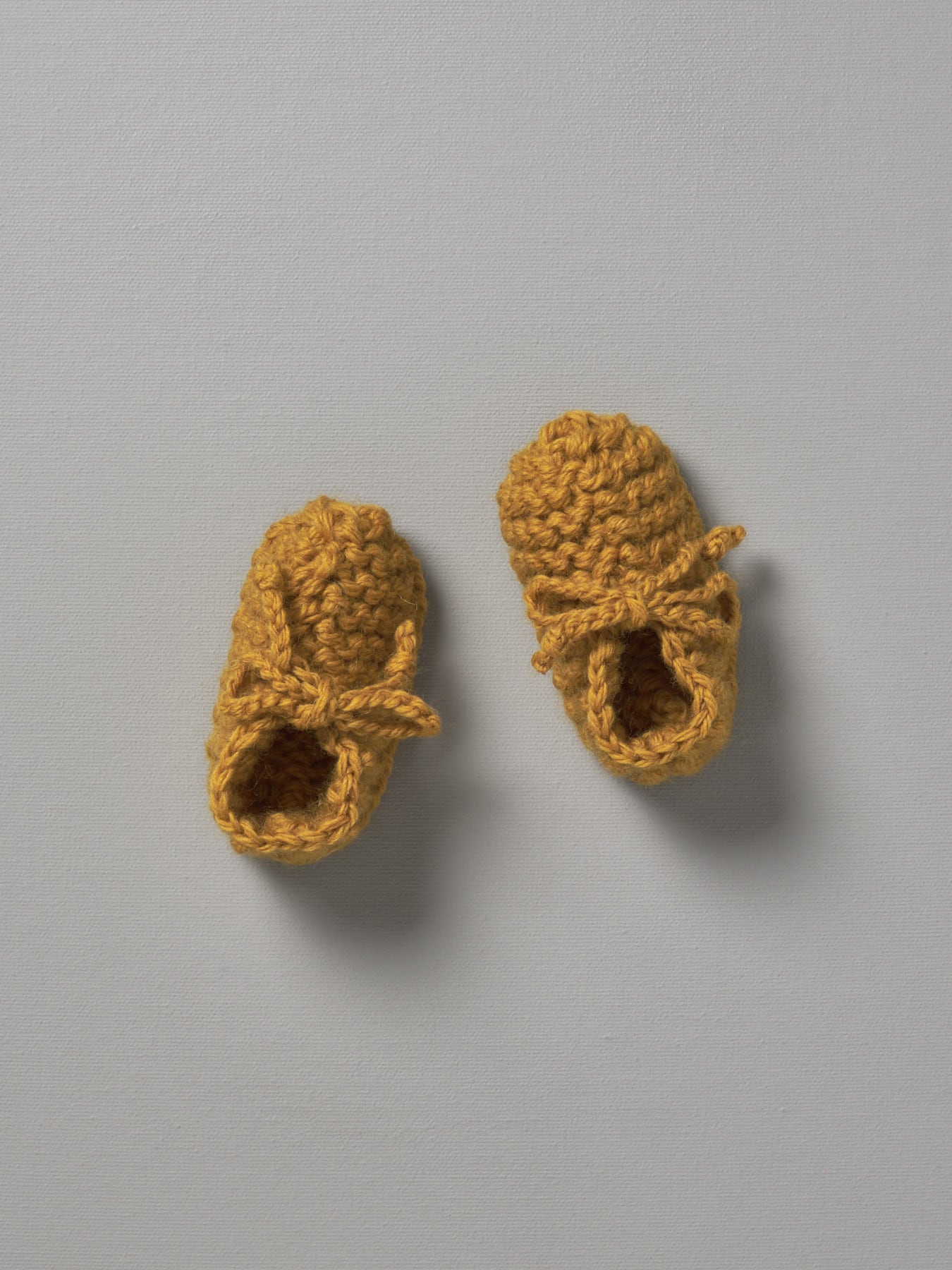 A pair of Weebits Hand Knitted Chunky Booties - Mustard baby shoes on a white surface.