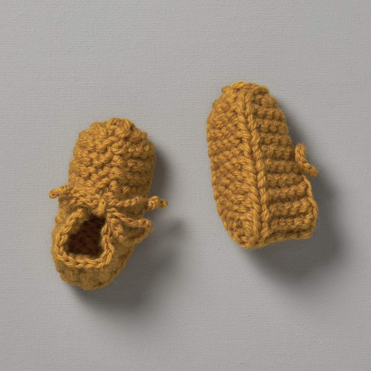 A pair of Weebits Hand Knitted Chunky Booties - Mustard on a grey surface.
