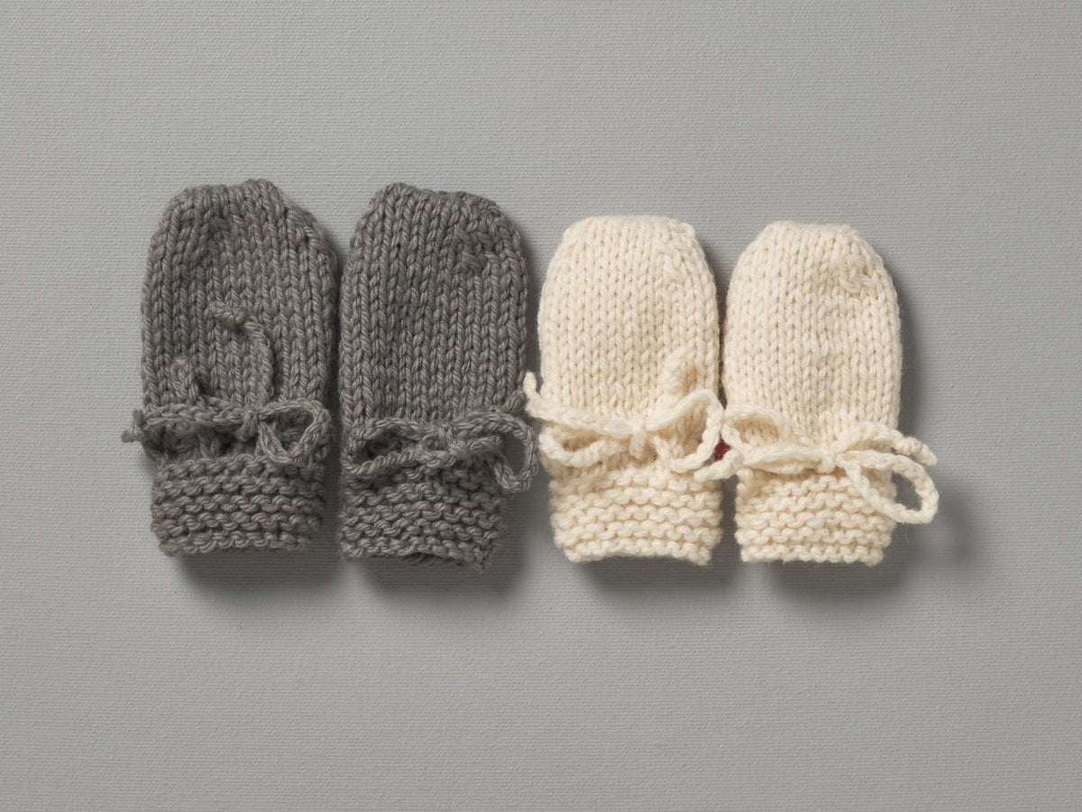 Three Weebits Hand Knitted Mittens - Natural on a grey surface.