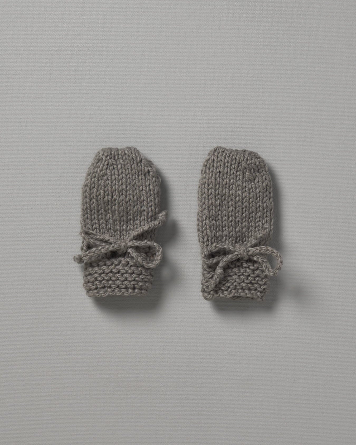 Two grey Weebits Hand Knitted Mittens on a white surface.