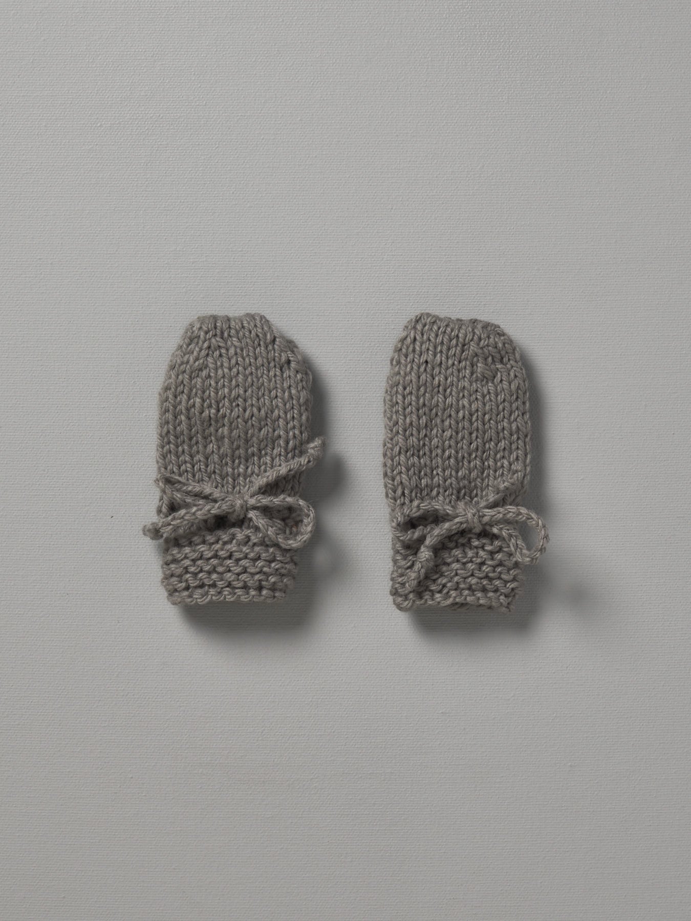 Two grey Weebits Hand Knitted Mittens on a white surface.