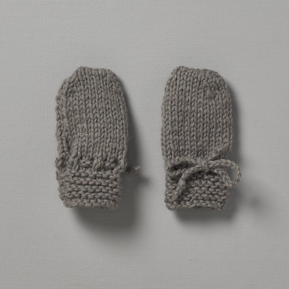 A pair of grey Weebits hand knitted mittens on a white surface.