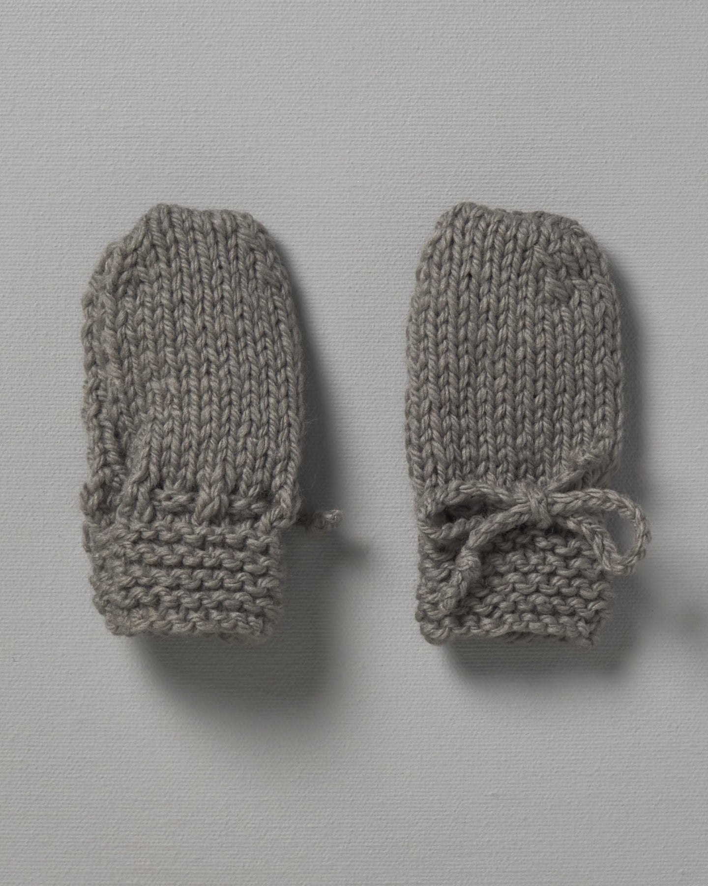 Two grey Weebits Hand Knitted Mittens on a white surface.