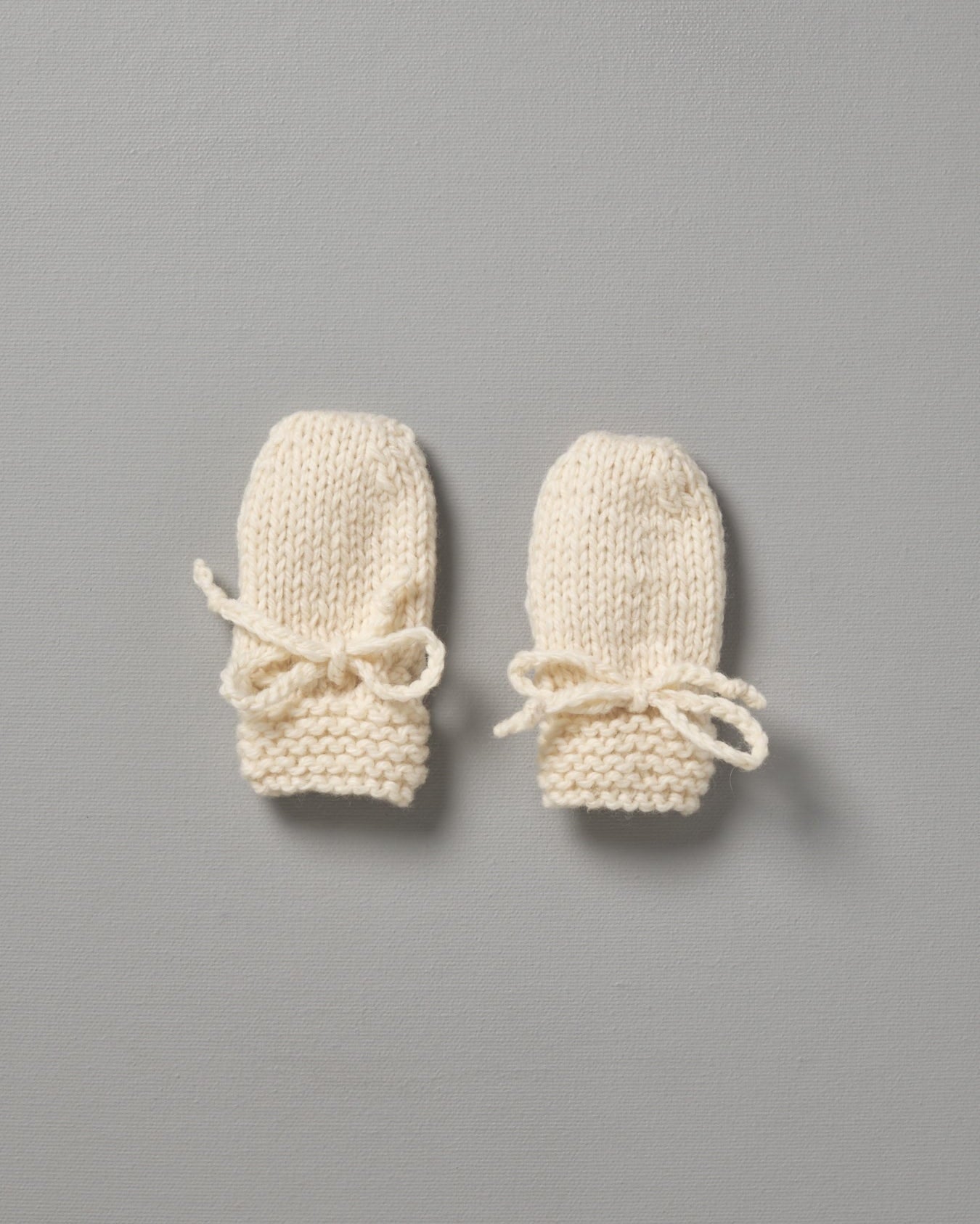 Two Weebits Hand Knitted Mittens on a grey background.