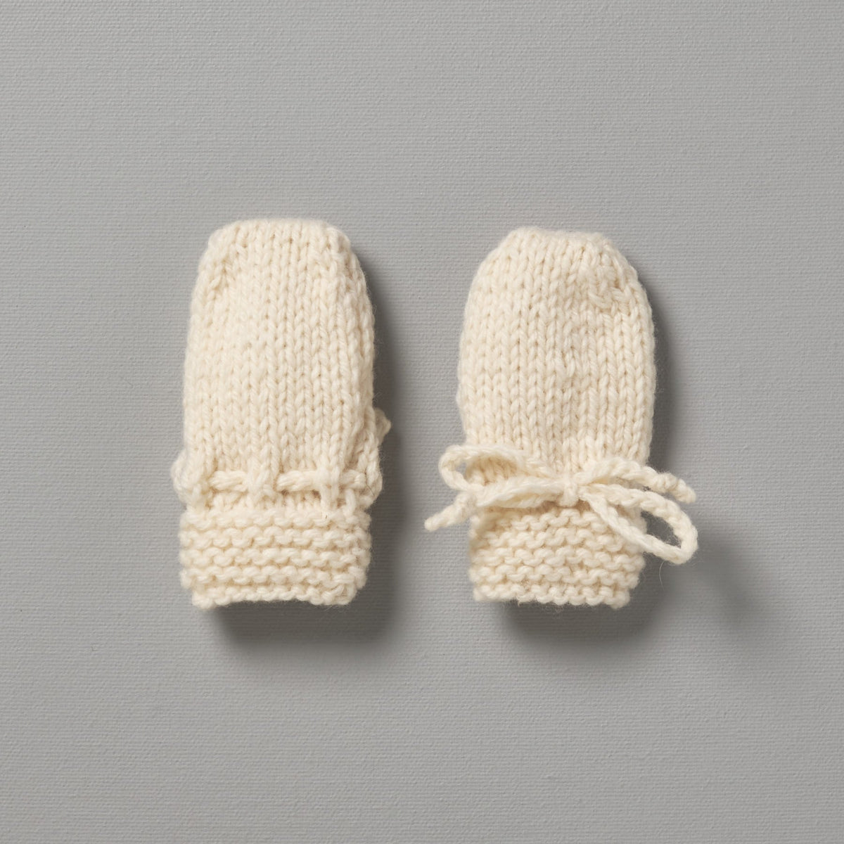 Two Weebits Hand Knitted Mittens - Natural on a grey surface.