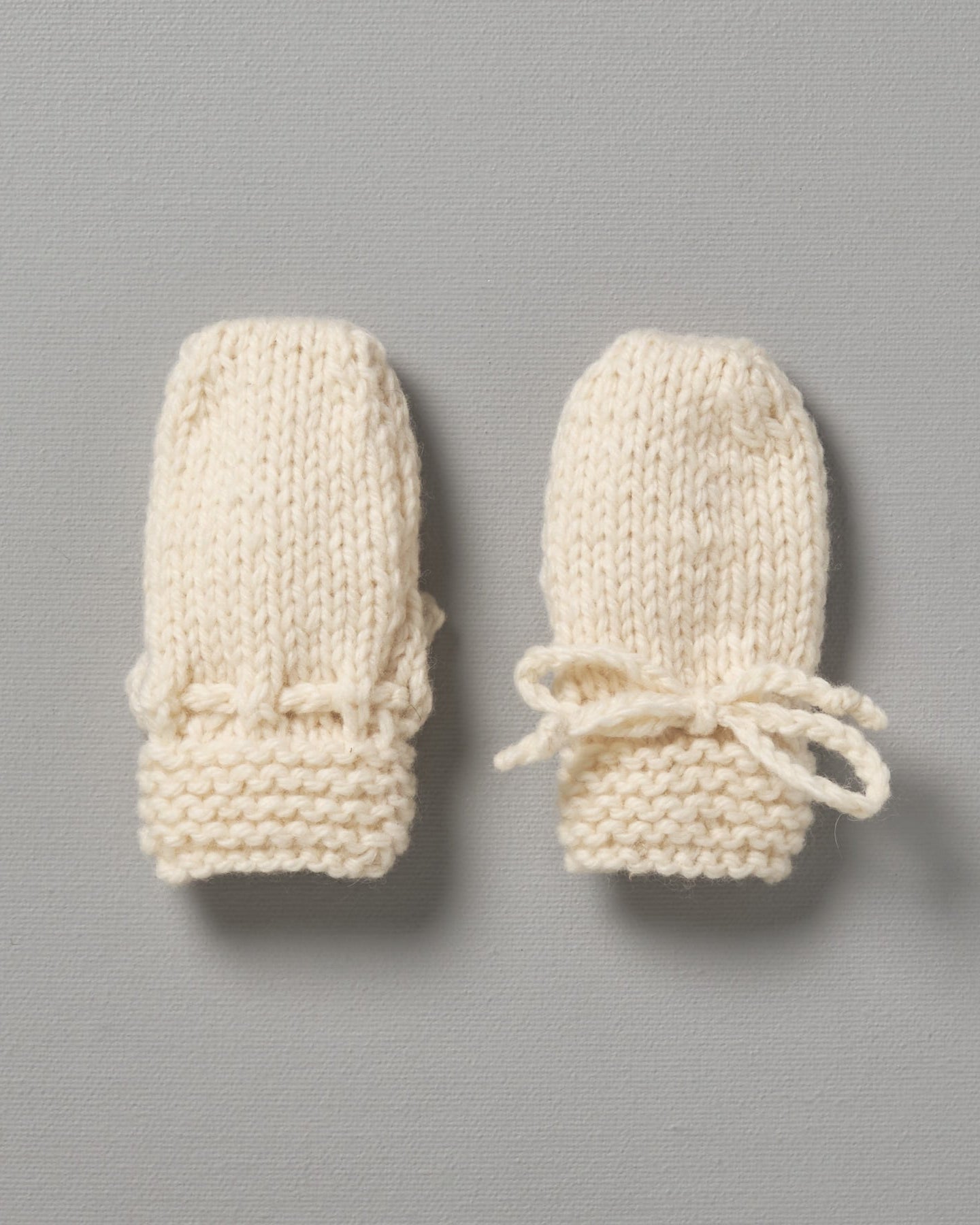 Two Weebits Hand Knitted Mittens on a grey background.