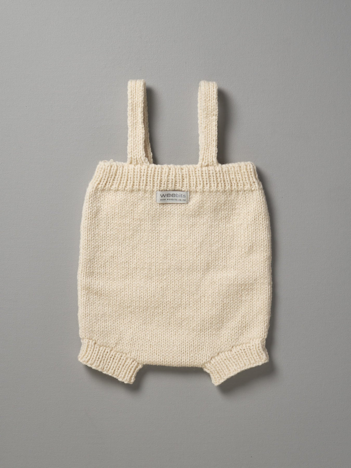 A Weebits Hand Knitted Romper - Natural on a grey background.