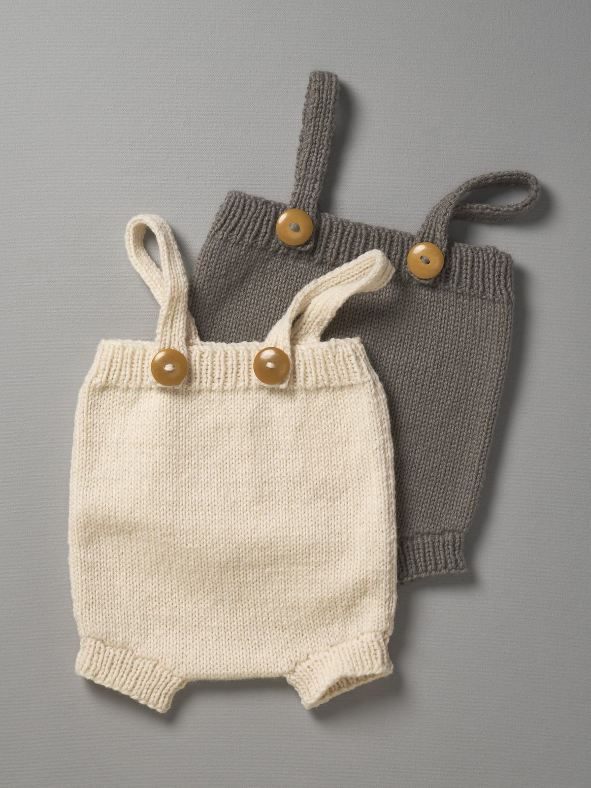 Two Weebits Hand Knitted Rompers - Natural on a grey surface.
