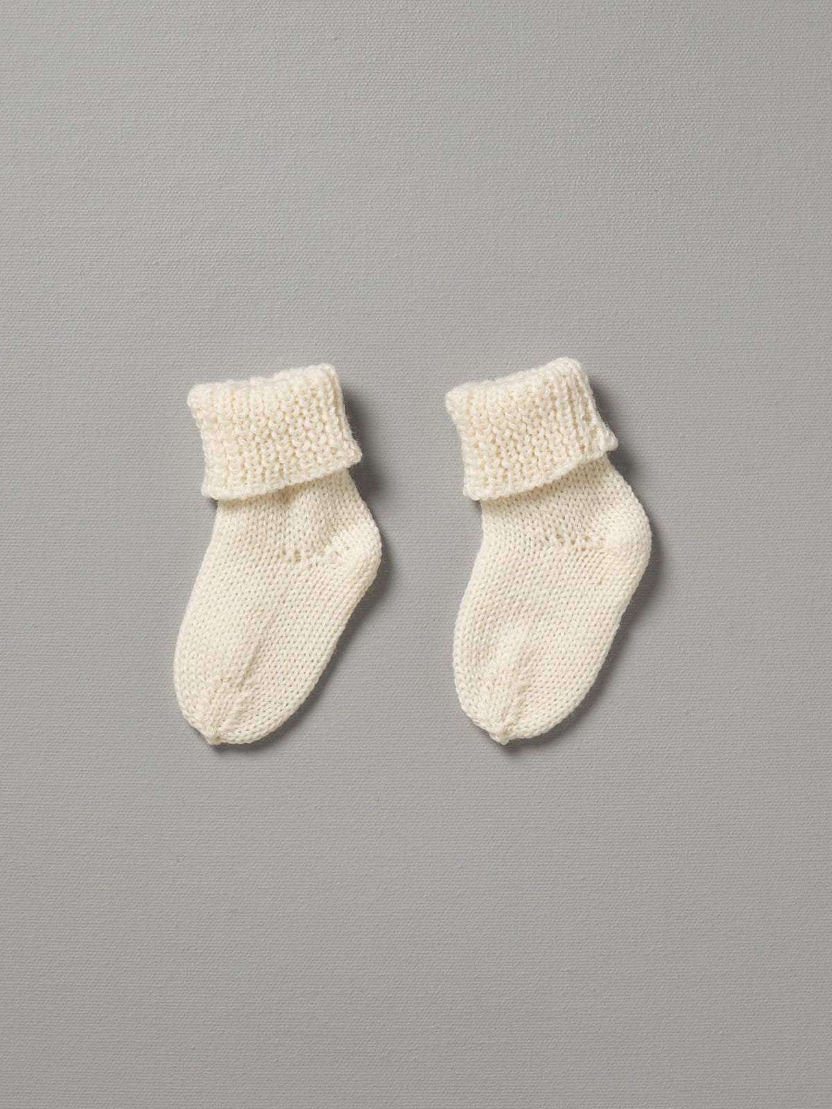 A pair of Weebits Hand Knitted 2ply Merino Socks  - Ivory on a grey background.