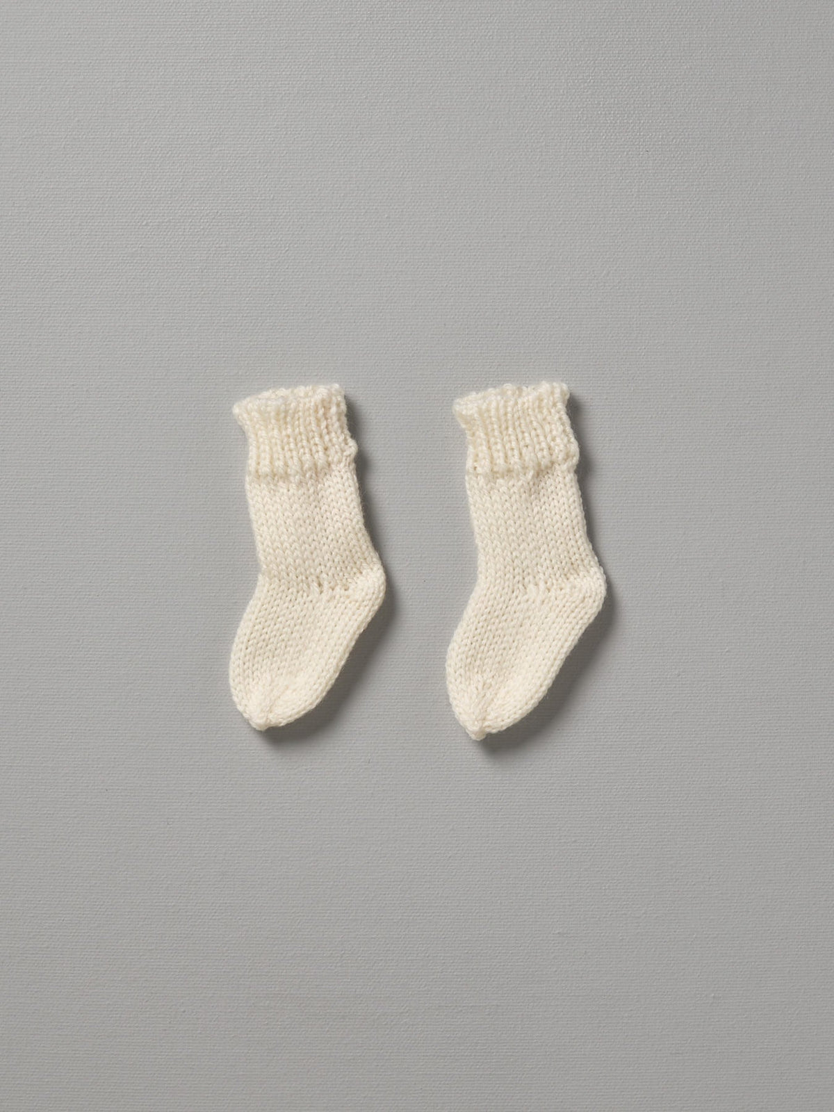 A pair of Weebits Hand Knitted 2ply Merino Socks - Ivory on a grey background.