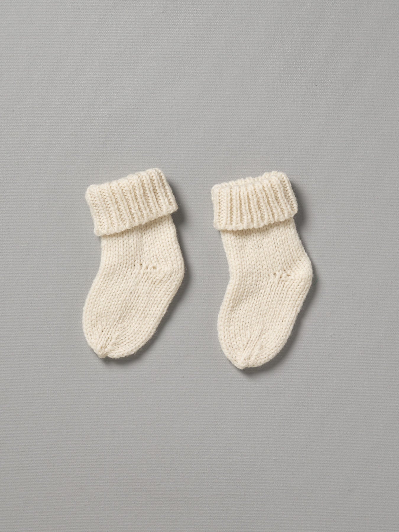 A pair of Weebits Hand Knitted 4ply Merino Socks in Ivory on a grey background.