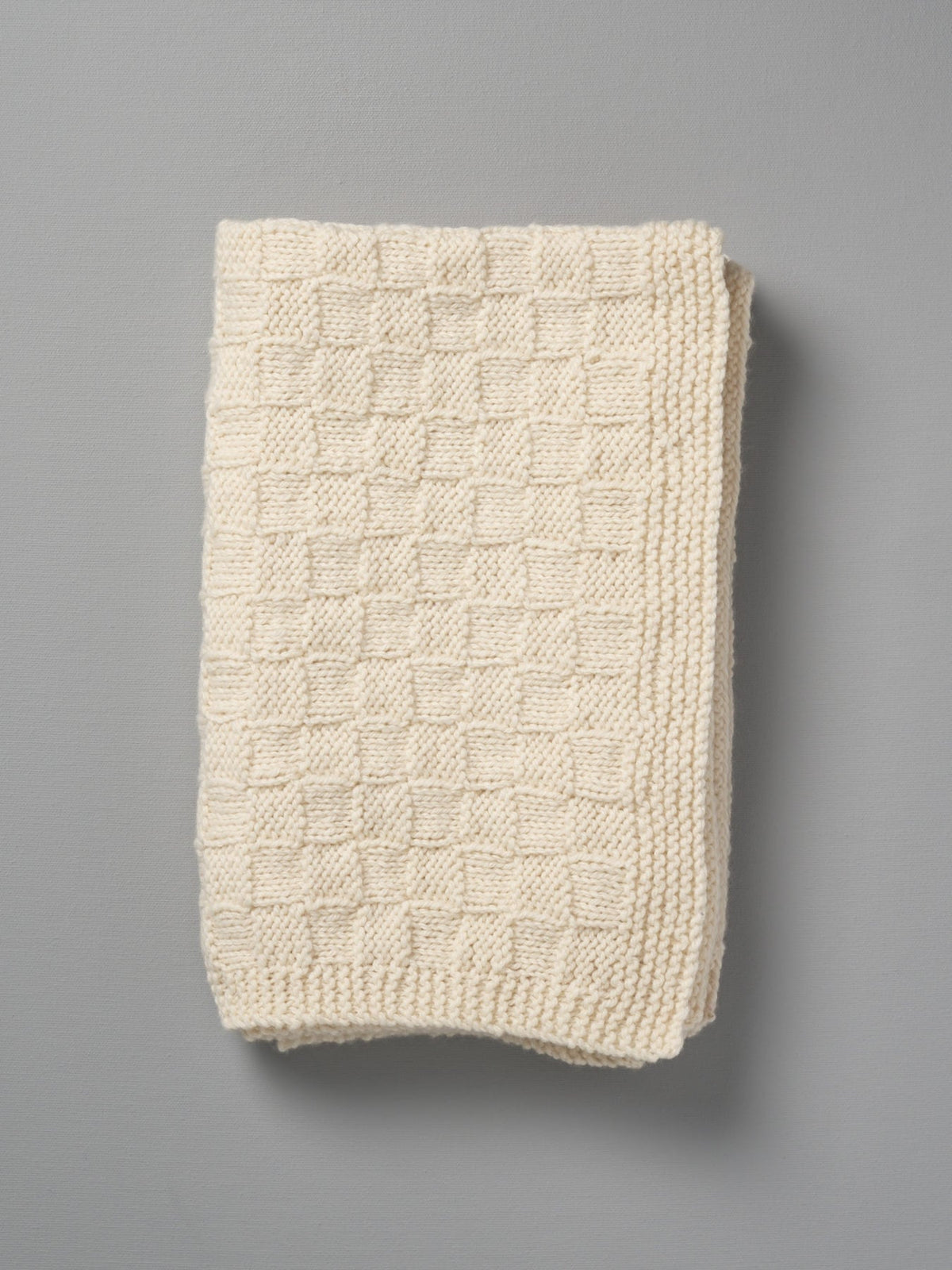 A Weebits Hand Knitted Travel Rug - Natural on a gray background.