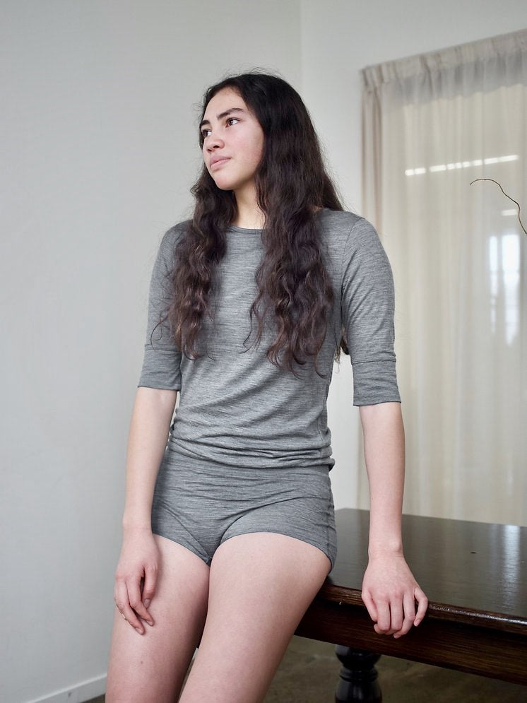 A young woman sitting on a table in YARN nz&#39;s Huia Merino Underpants - Grey.