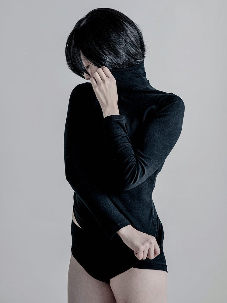 A woman wearing a Tui Fine Merino Rib Turtle - Black top by YARN nz and black shorts.