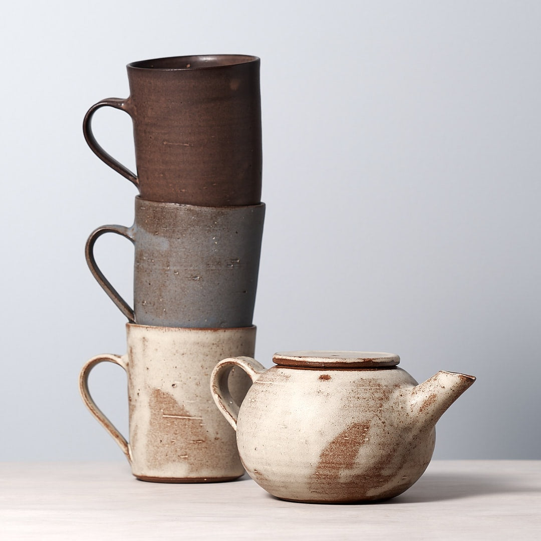 Three brown Zoë Isaacs mugs and a teapot stacked on top of each other.