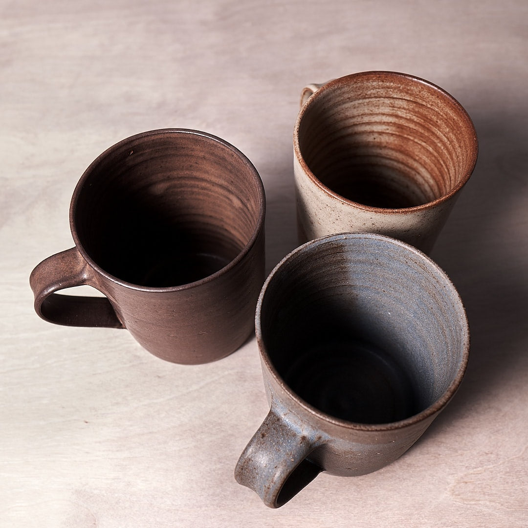 Three Zoë Isaacs Brown mugs sitting on a wooden surface.