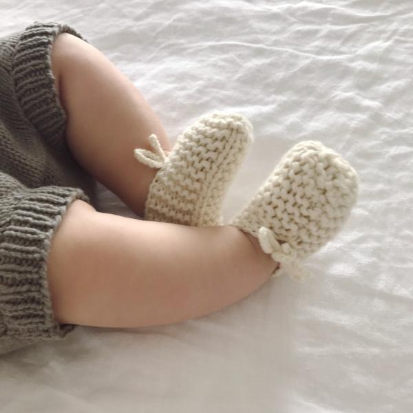 A baby is laying on a bed wearing a pair of Weebits Hand Knitted Chunky Booties - Mustard.