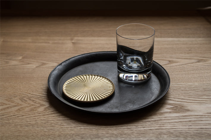 A Kobo Coaster – Solid Brass with a glass on it sits on a wooden table. [Brand Name: Futagami]