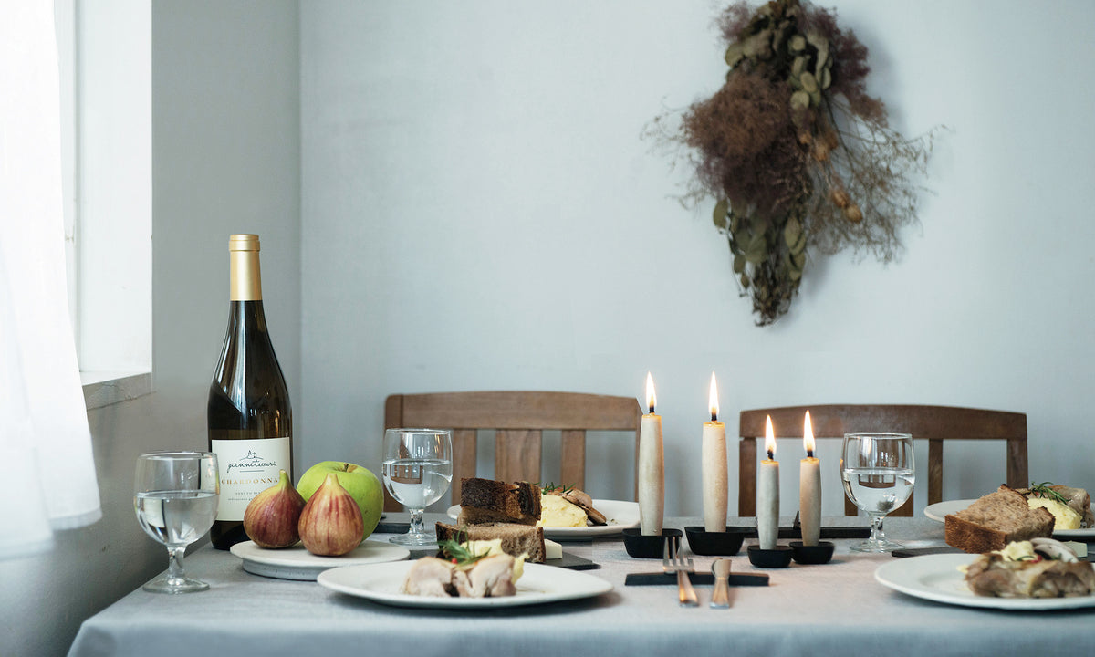 A table setting with Takazawa Koma Iron Candles - Large, wine and fruit.