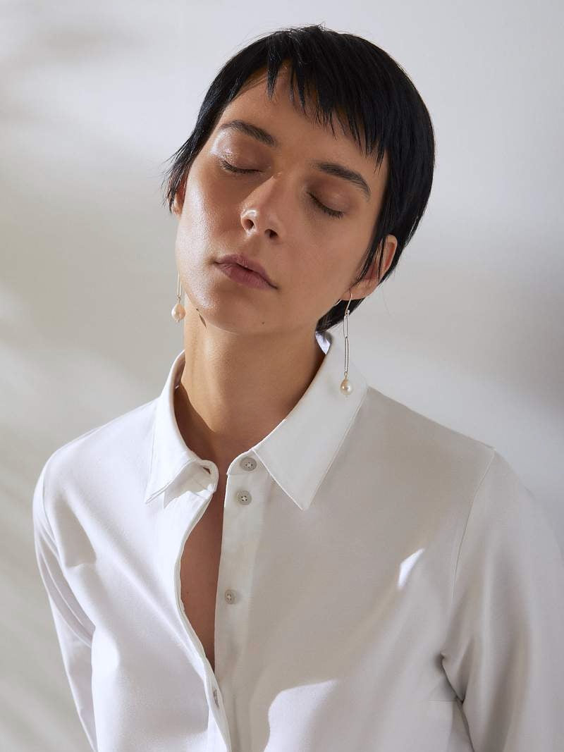 A woman wearing Baroque Pearl Earrings from EMBR Jewellery, a white shirt, and black pants.